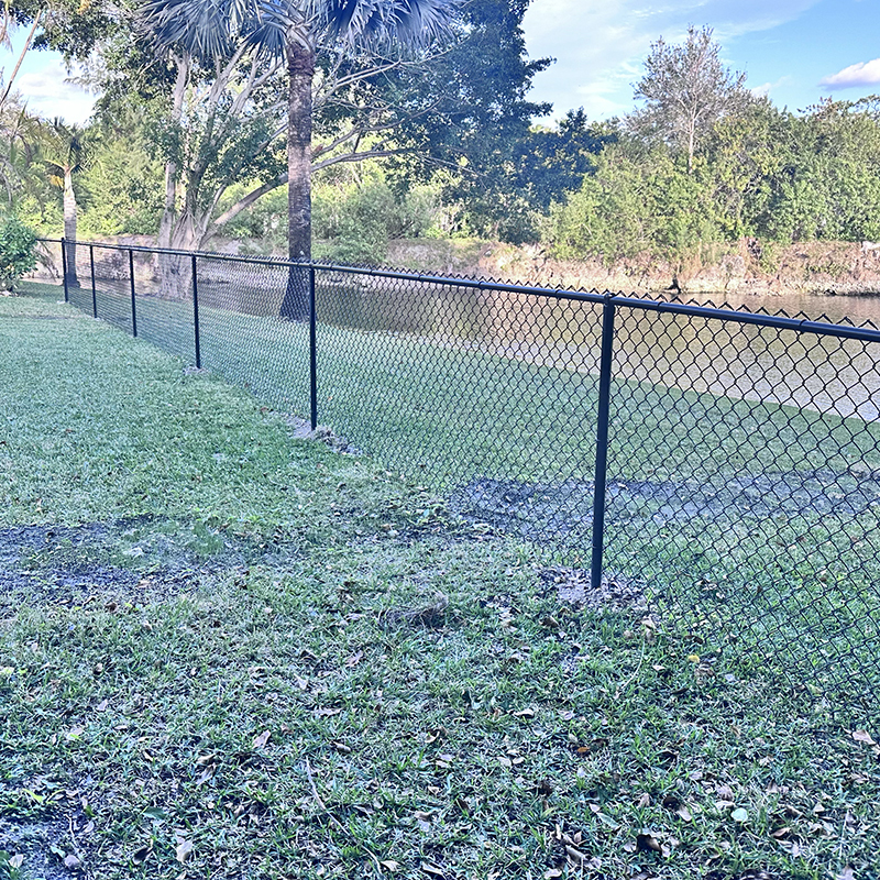 Recently installed black vinyl-coated chain link fence bordering a grassy yard in Parkland, FL, by Atanda Fence of South Florida.