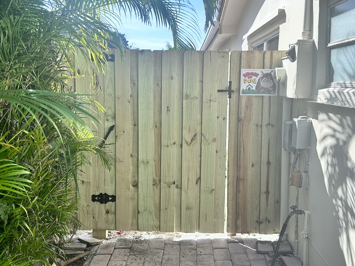 New wooden privacy fence gate with black hinges and latch installed beside a home in Plantation, FL, by Atanda Fence of South Florida.