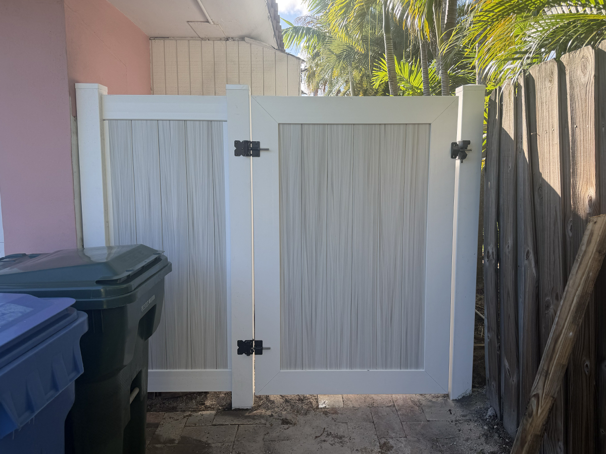 Two-tone Aspen PVC privacy fence gate with white framing and black hinges at a residential property in Oakland Park, FL.